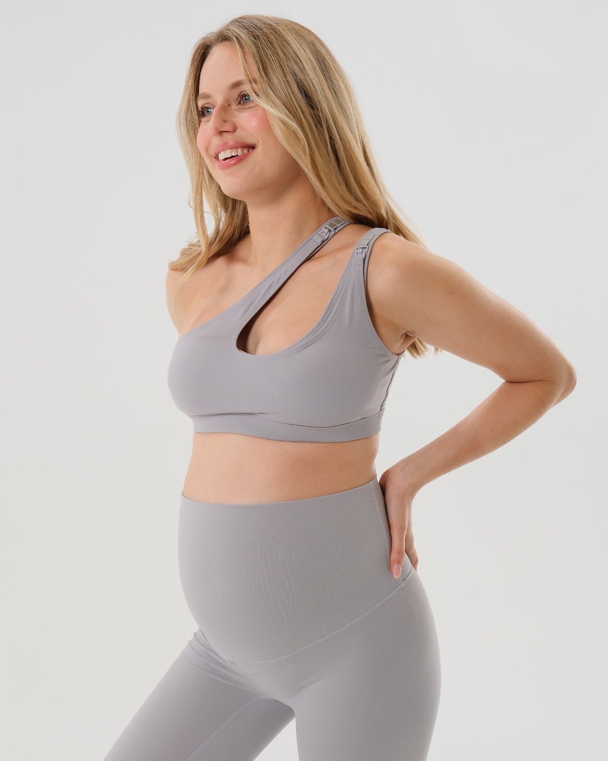 Light gray one-shoulder maternity and nursing sports bra and matching leggings. The bra features one-handed clip access for easy breastfeeding. Premium maternity activewear by AXK is offered in petite and plus size.