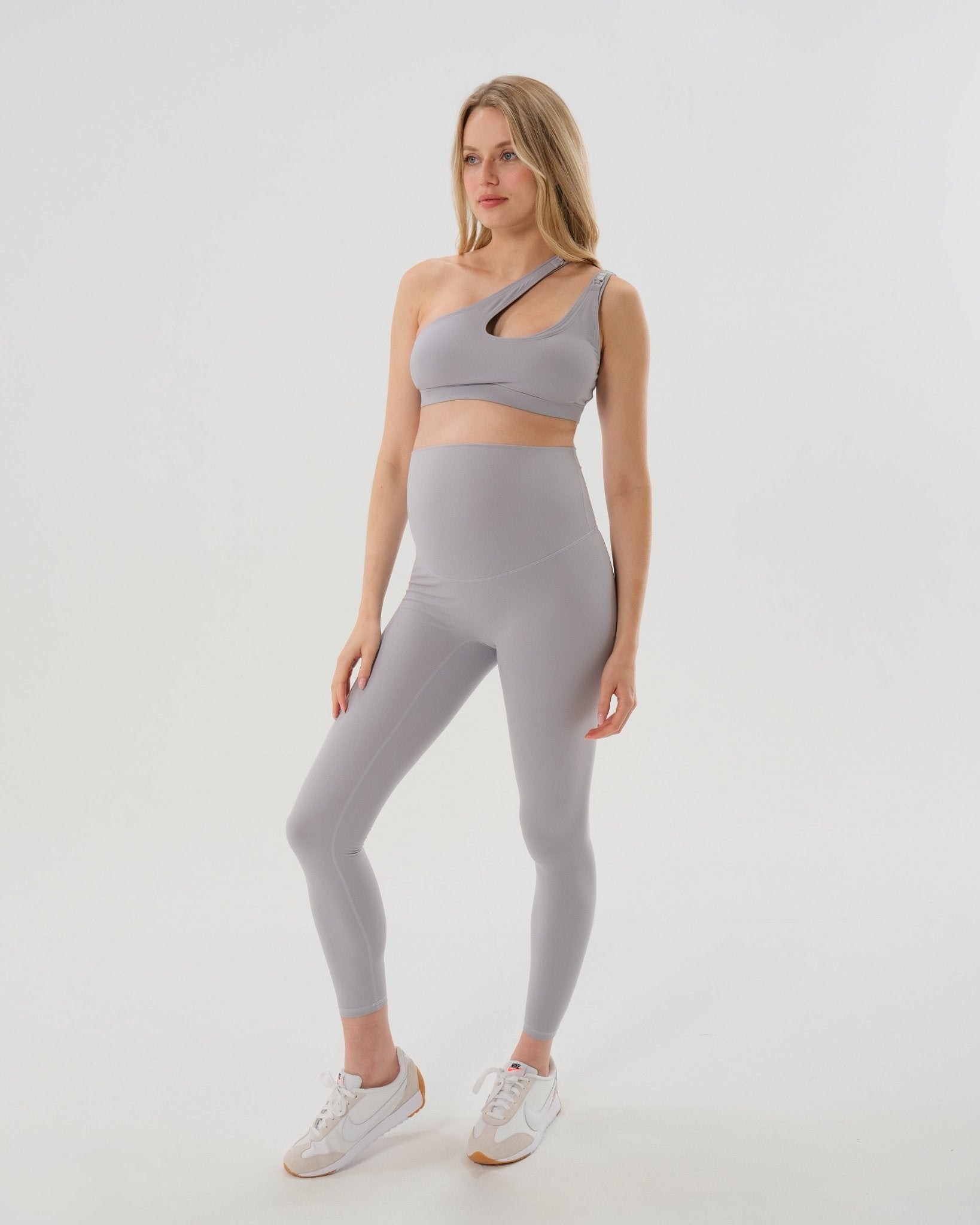 Pregnant woman wearing premium light grey maternity leggings with a flattering scrunch butt and supportive high waist and a high impact, racer back nursing sports bra on a white background. Premium maternity athletic and activewear by AXK - petite, tall and plus size friendly.
