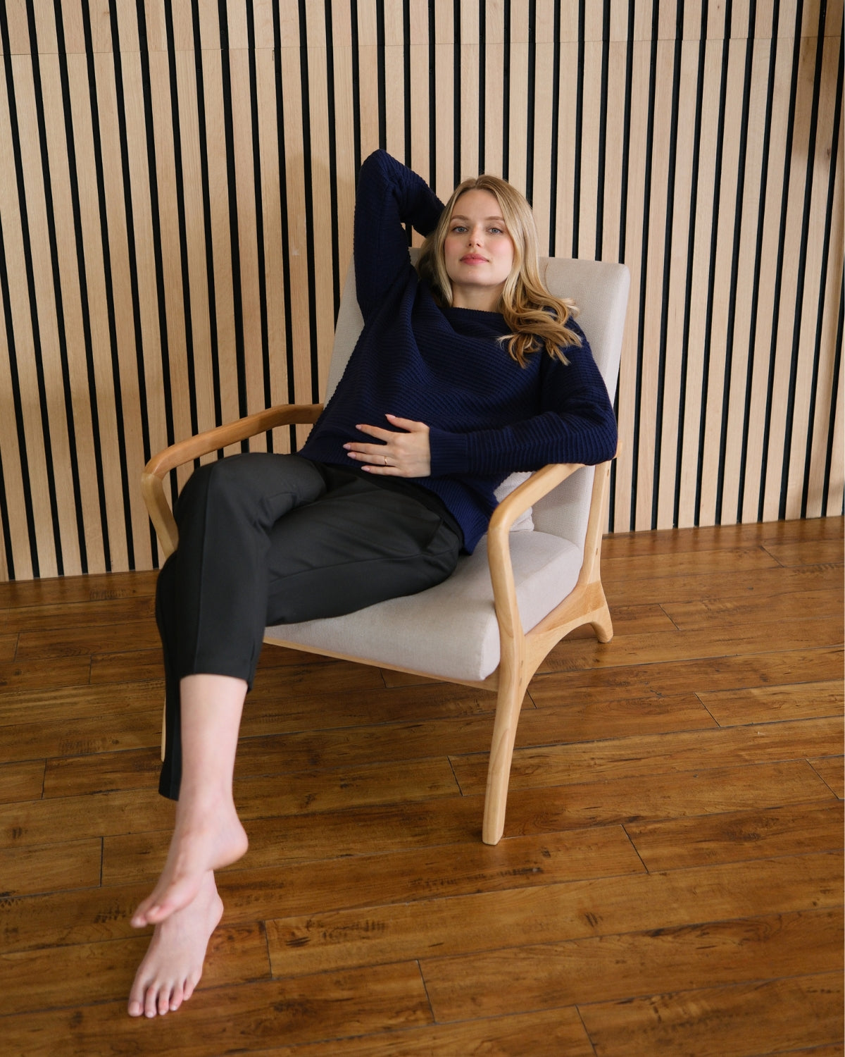 Navy neutral premium maternity and nursing sweater in stretch cotton box knit. Featuring shoulder button detail for breastfeeding and discreet hem thumbholes for an extra cozy fit. Oversized fit is flattering, polished, and versatile - transitioning from pregnancy workwear to loungewear to streetwear with ease. Petite and tall friendly; available in regular and plus size. Pictured with black Italian suiting cigarette pants. Lifestyle.