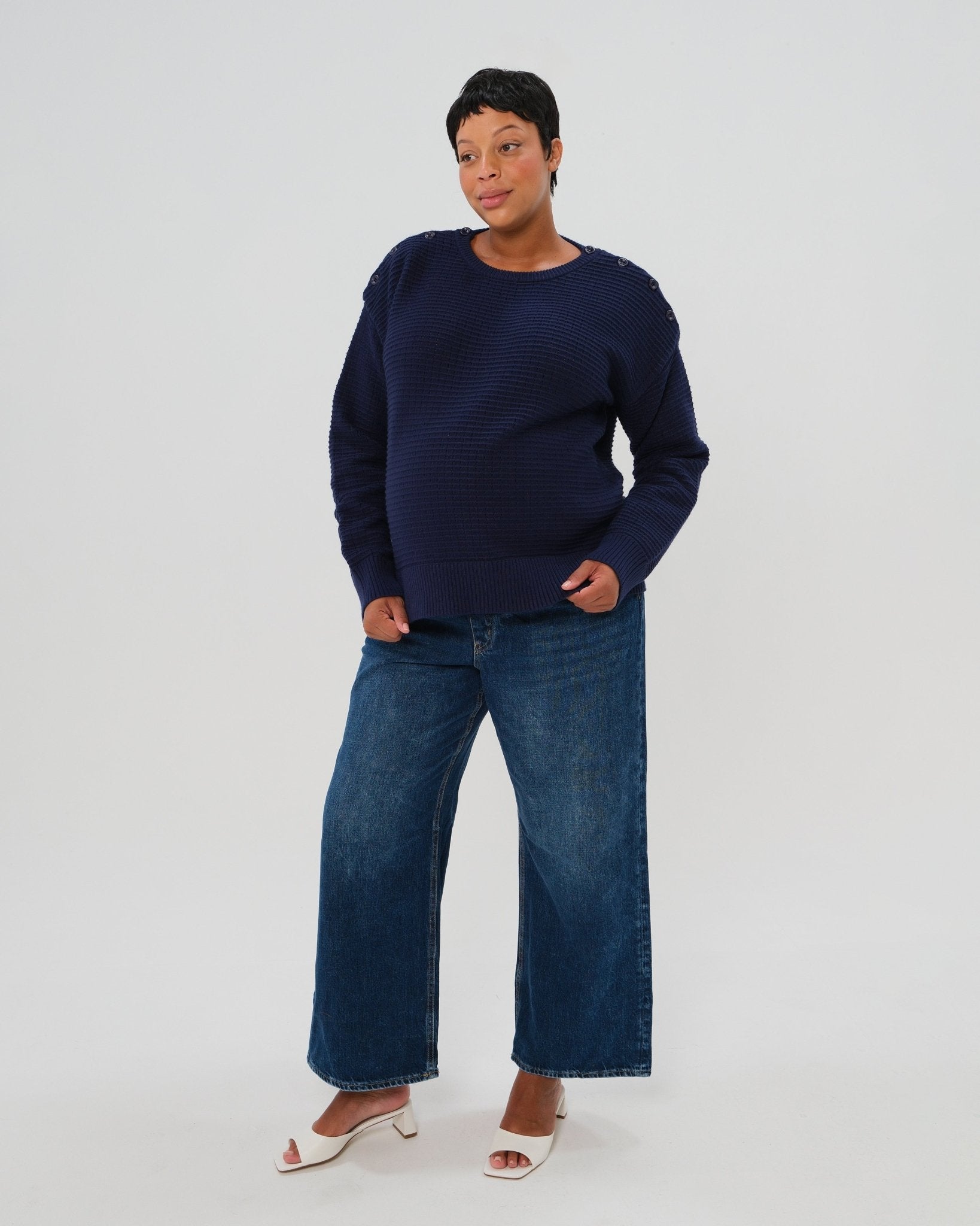 Navy premium maternity and nursing sweater in stretch cotton box knit. Featuring shoulder button detail for breastfeeding and discreet hem thumbholes for an extra cozy fit. Oversized fit is flattering, stylish, and versatile - transitioning from pregnancy workwear to loungewear to street wear with ease. Petite and tall friendly; available in regular and plus size. Pictured with wide leg maternity jeans and sandals.