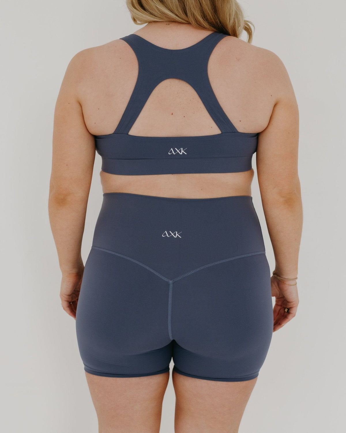 Pregnant woman wearing premium blue maternity bike shorts with a supportive high waist and matching high-impact, racerback maternity and nursing sports bra. Premium maternity athletic and activewear by AXK in petite friendly and plus sizes.