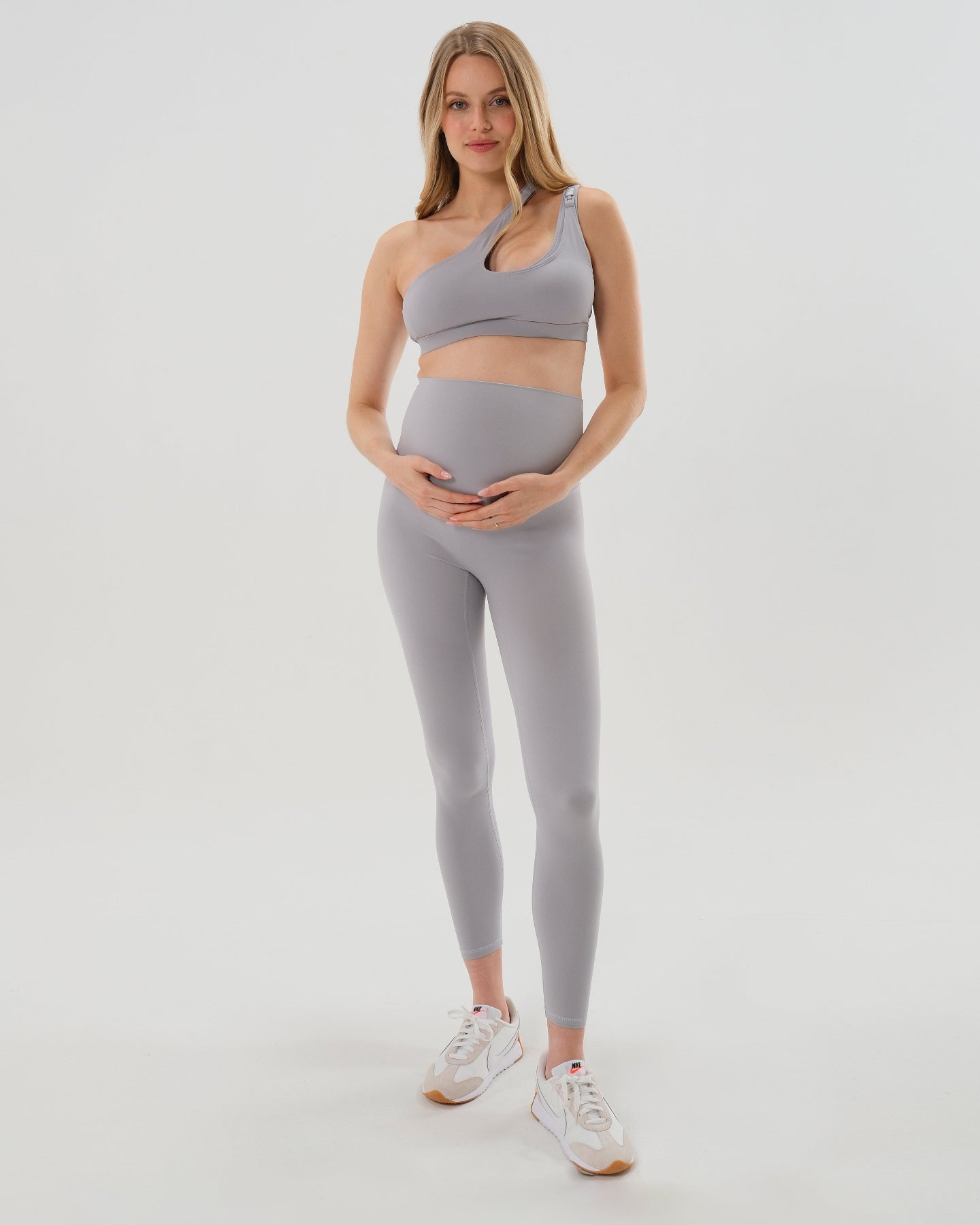 Pregnant model wearing premium light gray AXK maternity leggings with a supportive high waist, bum flattering back v seam, seamless front design, and butter soft stretch fabric. Best selling with glowing 5-star reviews, these leggings are perfect for running, pregnancy yoga, walking, biking, or loungewear. High quality 2026 maternity athletic and activewear in regular and plus sizes. Petite and tall friendly. 