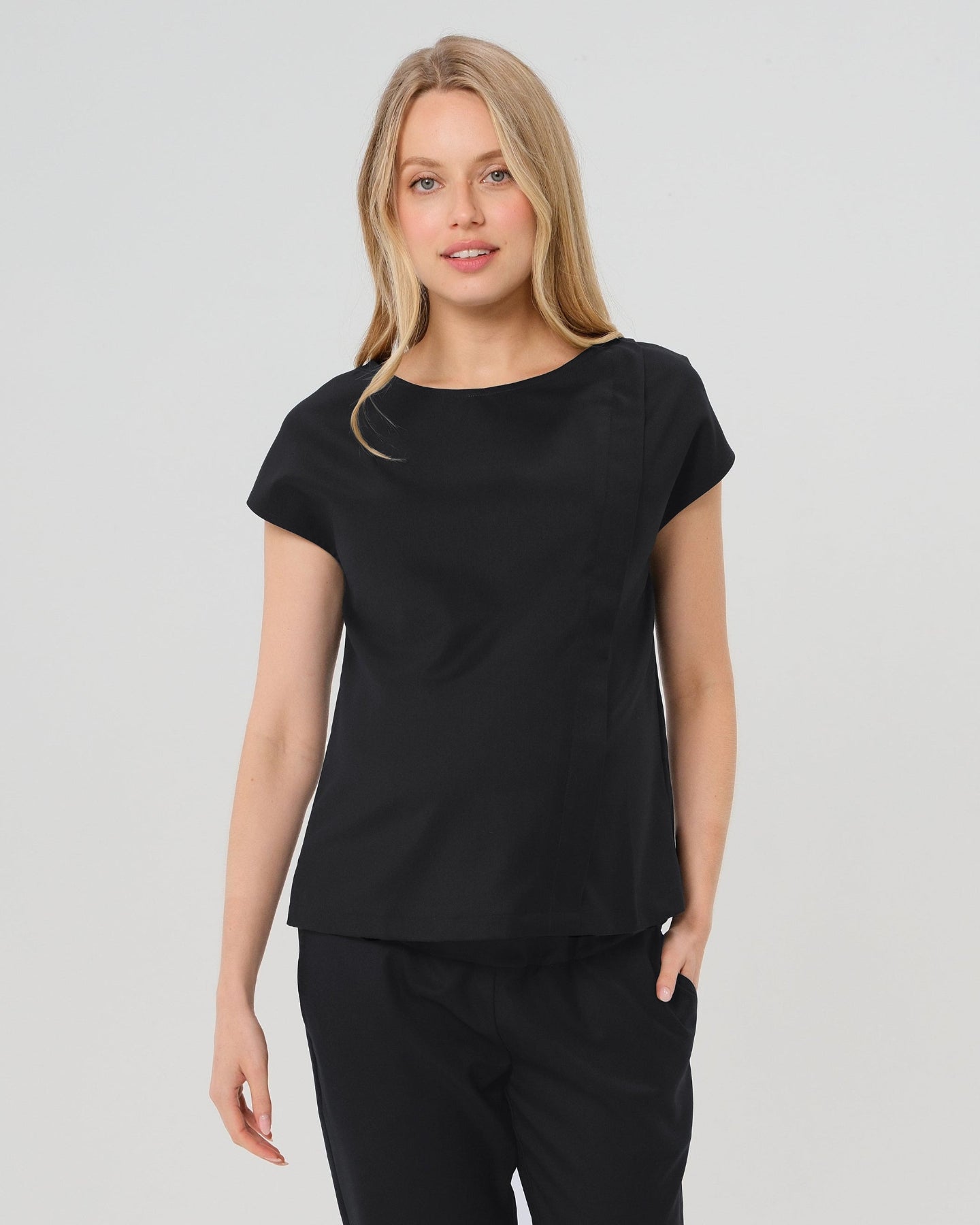 Pregnant woman wearing a black maternity short sleeve boat neck shell top with designer nursing zipper and easy, flattering elegance for work or going out. Cut in breathable, all-season tropical wool blend. This bestselling business apparel item features cap sleeves perfect for spring and summer pregnancy or breastfeeding; transitions perfectly for layering under jackets or sweaters in fall and winter. Available in regular and plus sizes. Petite and tall friendly. 