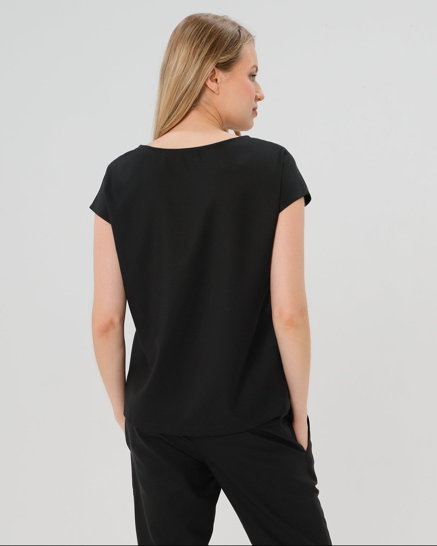 Back view of black short sleeve designer maternity and nursing shell top in breathable tropical wool blend. This best - in - class pregnancy business attire or streetwear style with glowing parent expo reviews is sure to be one of the most sought after designs of 2026. Perfect for work, occasions, outings, and more, the cut is flattering and comfortable, with the diagonal zipper providing the perfect discreet breastfeeding zipper. 