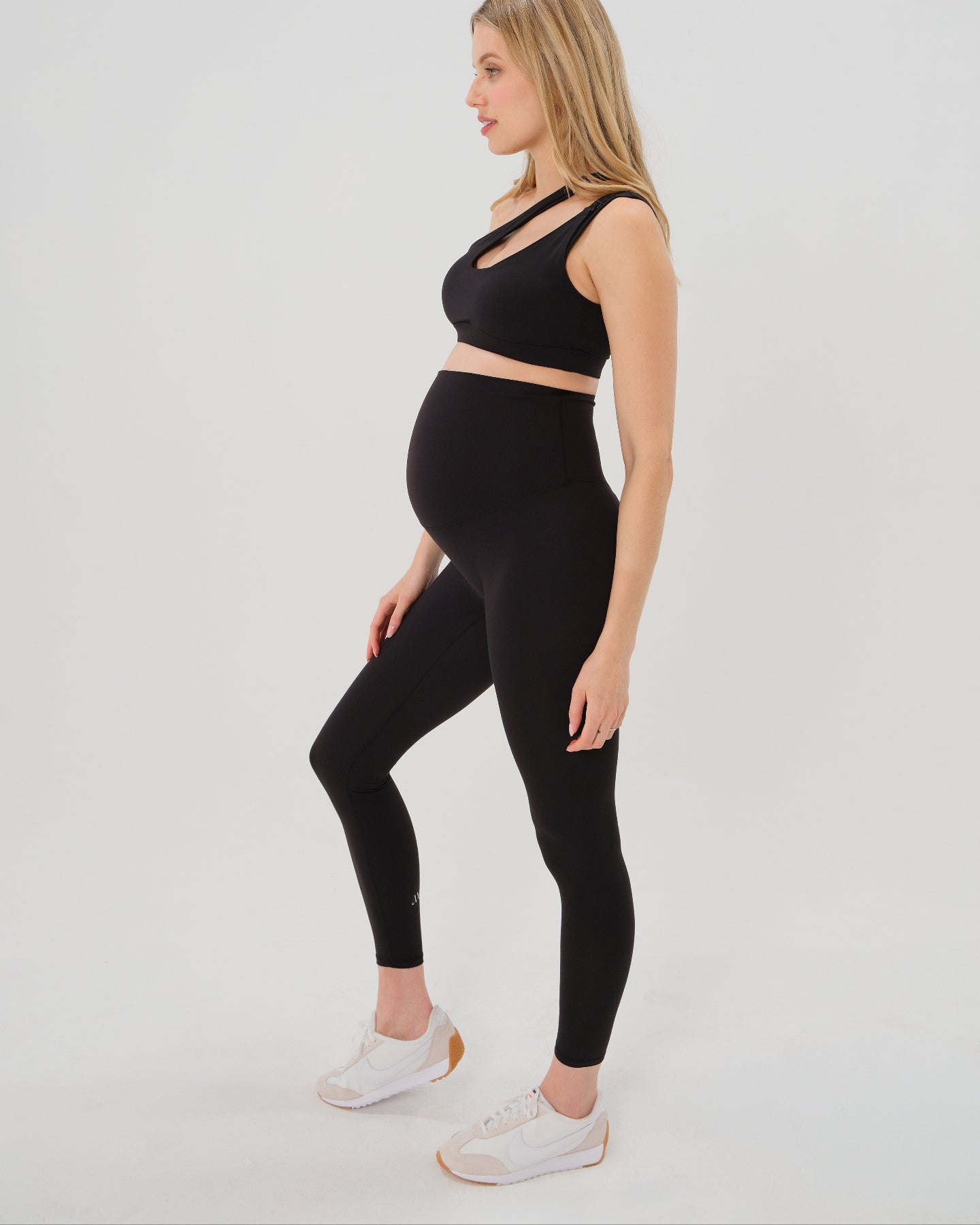 Pregnant model wearing premium black AXK maternity leggings with a supportive high waist, bum flattering back v seam, seamless front design, and butter soft stretch fabric. Best selling with glowing 5-star reviews, these leggings are perfect for running, pregnancy yoga, walking, biking, or loungewear. High quality 2026 maternity athletic and activewear in regular and plus sizes. Petite and tall friendly. 