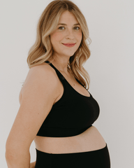 Side view of a pregnant woman wearing a black high-impact, racerback, maternity and nursing sports bra paired with matching high-waist leggings. Premium maternity athletic and activewear by AXK.