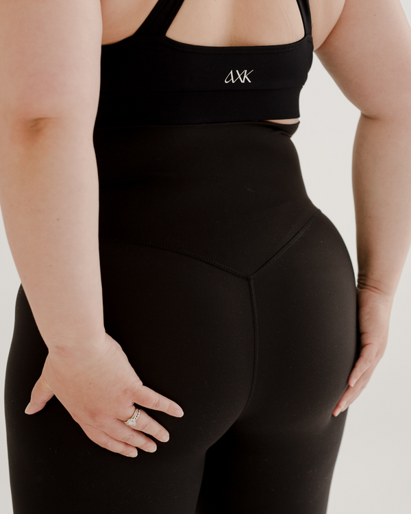 Close-up back view of premium black maternity leggings with a supportive high waist and V-seam detail, paired with a high-impact, racerback maternity and nursing sports bra. Premium maternity athletic and activewear by AXK.