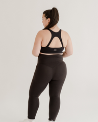 Back view of a pregnant woman wearing premium black maternity leggings with a supportive high waist and matching high-impact, racerback, maternity and nursing sports bra, standing against a white background. Premium maternity athletic and activewear by AXK.