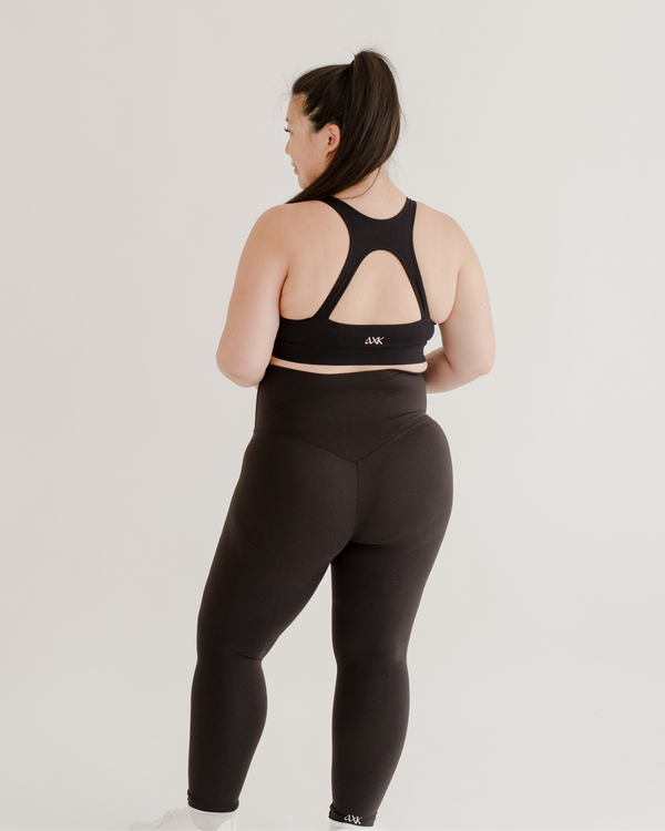 Back view of a pregnant woman wearing premium black maternity leggings with a supportive high waist and matching high-impact, racerback, maternity and nursing sports bra, standing against a white background. Premium maternity athletic and activewear by AXK.