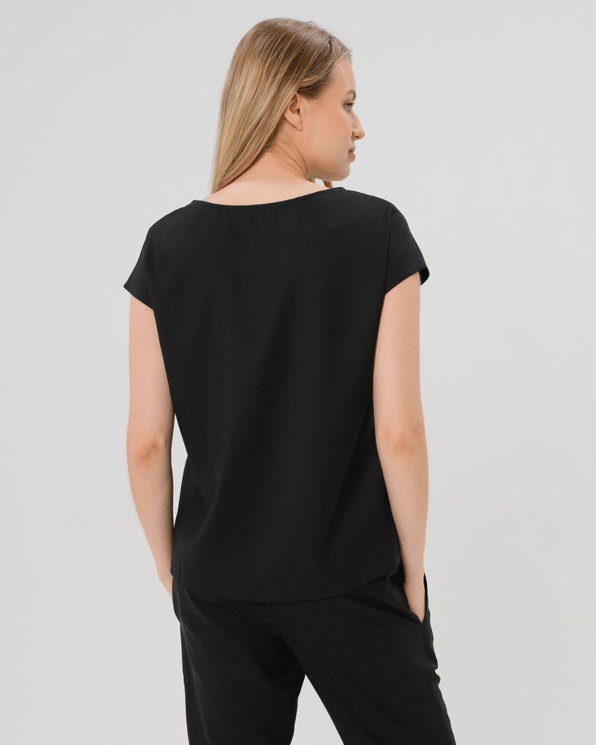 Pregnant woman wearing a black maternity short sleeve boat neck shell top with designer nursing zipper and easy, flattering elegance for work or going out. Cut in breathable, all-season tropical wool blend. This bestselling business apparel item features cap sleeves perfect for spring and summer pregnancy or breastfeeding; transitions perfectly for layering under jackets or sweaters in fall and winter. 