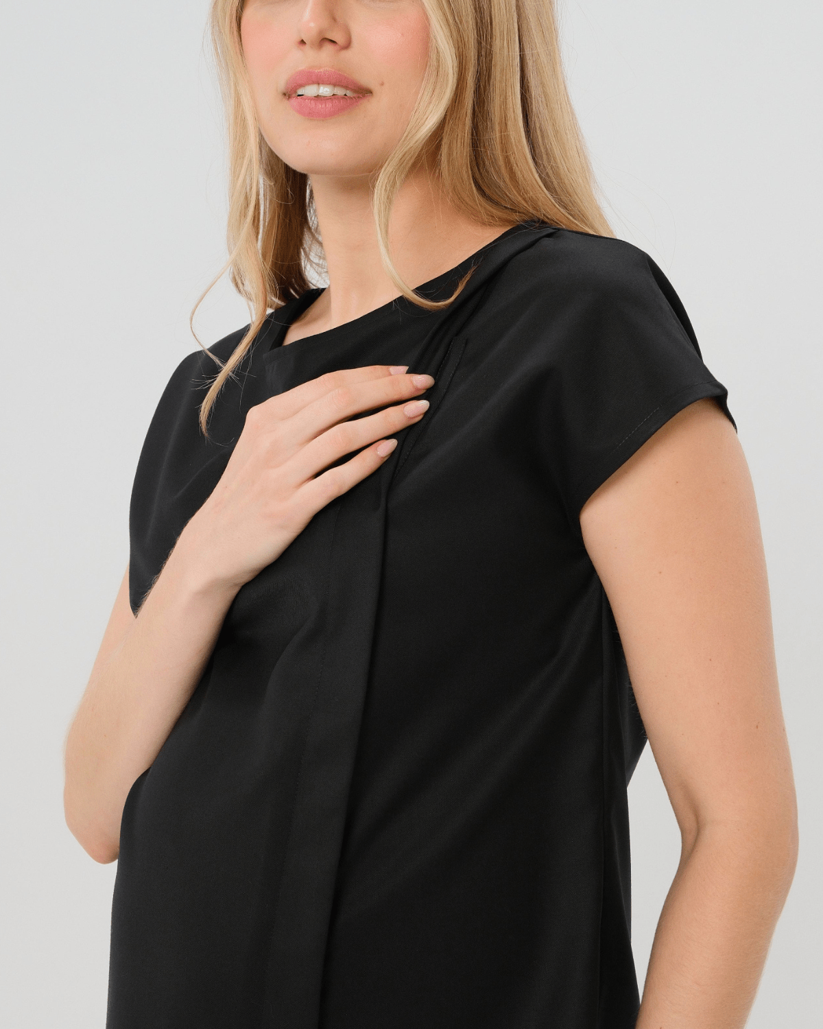 Pregnant woman wearing a black maternity short sleeve boat neck shell top with designer nursing zipper and easy, flattering elegance for work or going out. Cut in breathable, all-season tropical wool blend. This bestselling business apparel item features cap sleeves perfect for spring and summer pregnancy or breastfeeding; transitions perfectly for layering under jackets or sweaters in fall and winter. Close up of nursing zipper.