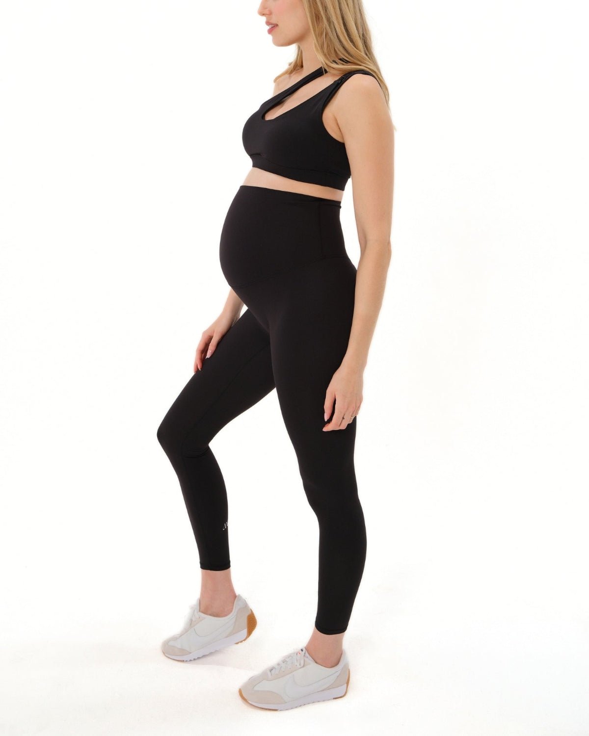 Pregnant woman wearing premium black maternity leggings with a flattering scrunch butt and matching high-impact, racerback nursing sports bra, standing against a white background. Premium maternity athletic and activewear by AXK.