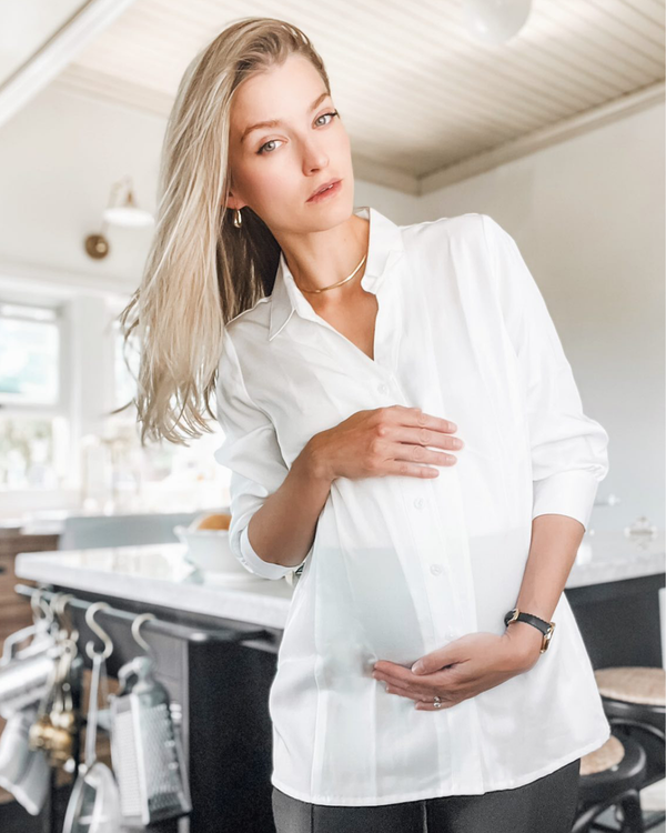 White maternity button down shirt for pregnancy and nursing by MARION. Maternity workwear top with no gap technology that prevents your bra from showing. Cut with luxury sustainable TENCEL, this classic blouse is ideal for a business meeting at the office, the courtroom, or Saturday errands and brunch. Available in petite and regular sizes, and made for pregnancy, nursing, postpartum, and mama life. 
