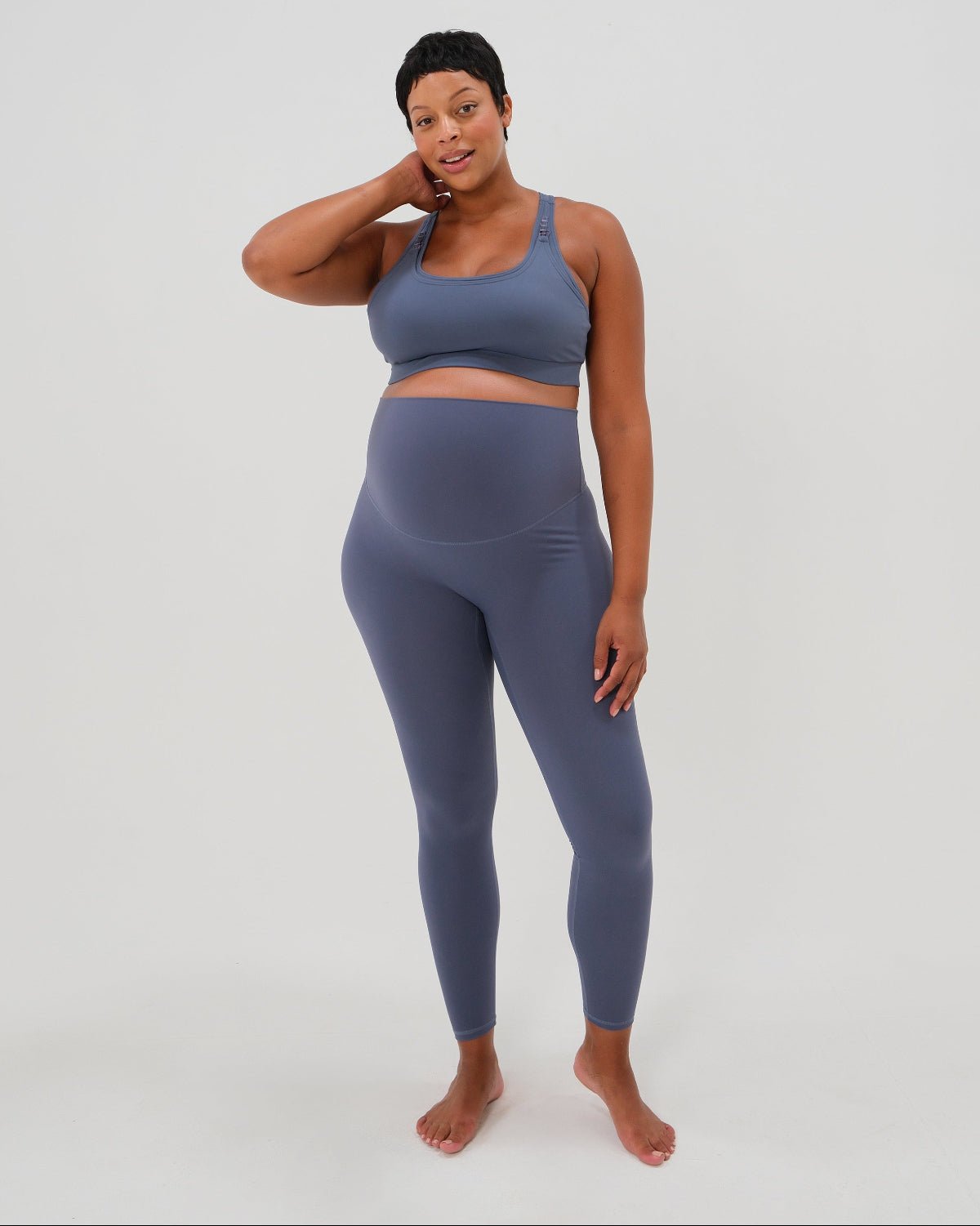 Pregnant woman wearing premium blue maternity leggings with a flattering scrunch butt and matching high-impact, racerback nursing sports bra, standing against a white background. Premium maternity athletic and activewear by AXK.