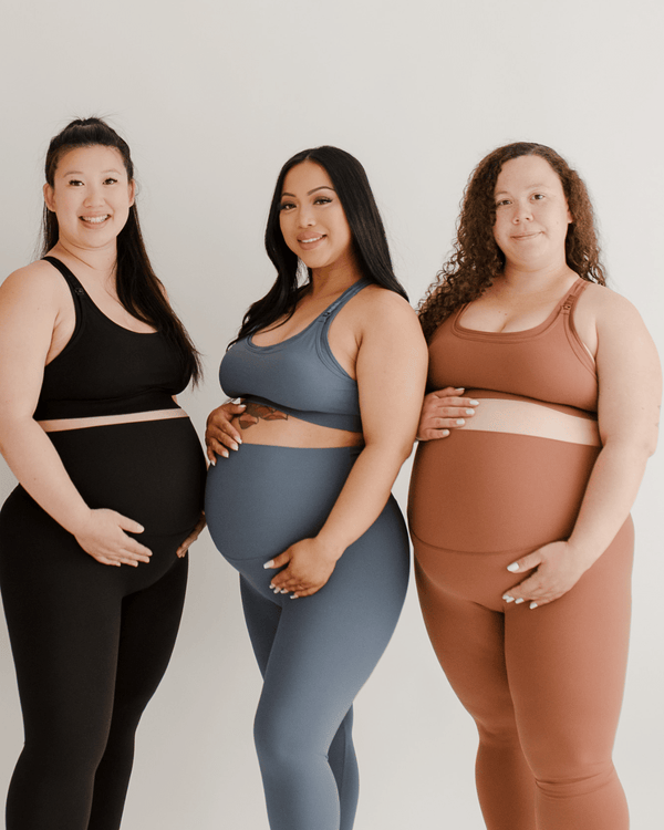 Three pregnant women wearing AXK maternity leggings and matching high-impact, racerback, maternity and nursing sports bras in black, blue, and brown, standing together against a white background. Premium maternity athletic and activewear by AXK.
