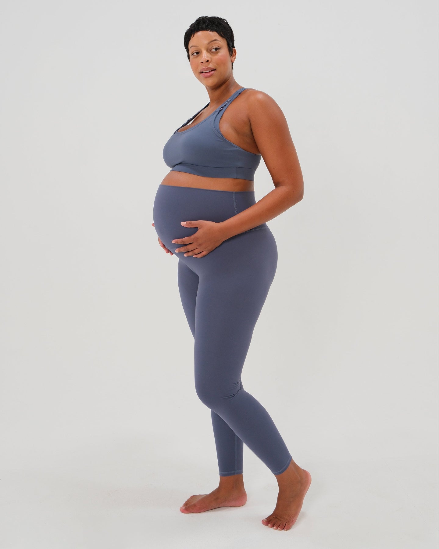 Pregnant plus size model wearing premium blue AXK maternity leggings with a supportive high waist, bum flattering back v seam, seamless front design, and butter soft stretch fabric. Best selling with glowing 5-star reviews, these leggings are perfect for running, pregnancy yoga, walking, biking, or loungewear. High quality 2026 maternity athletic and activewear in regular and plus sizes. Petite and tall friendly. 