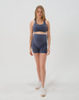 Pregnant woman wearing premium blue maternity bike shorts with a supportive high waist and matching high-impact, racerback maternity and nursing sports bra. Premium maternity athletic and activewear by AXK in petite friendly and plus sizes.