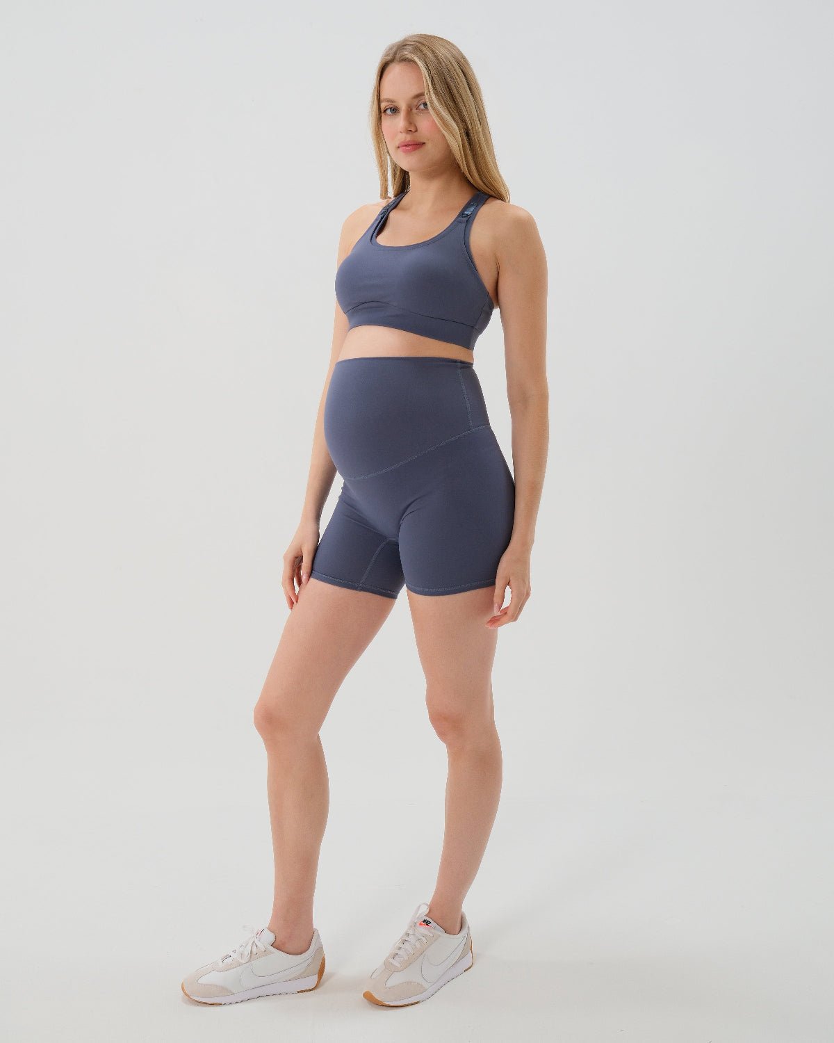 Pregnant woman wearing premium blue maternity bike shorts with a supportive high waist and matching high-impact, racerback maternity and nursing sports bra. Premium maternity athletic and activewear by AXK in petite friendly and plus sizes.