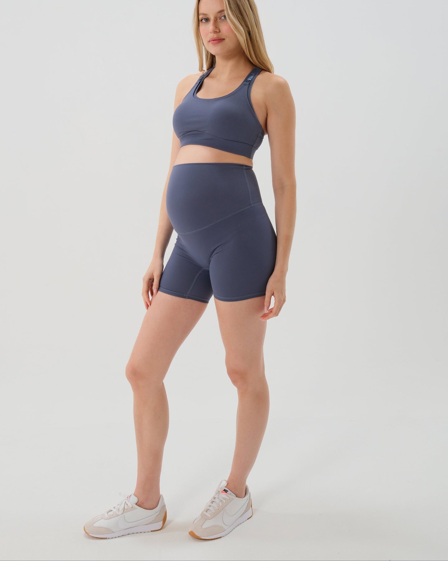 Pregnant woman wearing premium blue maternity bike shorts with a supportive high waist and matching high-impact, racerback maternity and nursing sports bra. Best reviewed 2026 premium maternity athletic and activewear by AXK, petite and tall friendly, in regular and plus size options. 