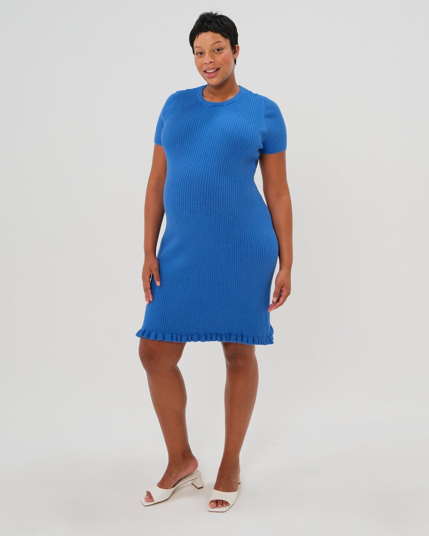 Beautiful plus size pregnant model wearing a high end vibrant blue knee length knit maternity dress. This dress features breathable luxury stretch cotton knit, a feminine hem ruffle, and easy crew neck. Garnering exceptional reviews, this best-in-class design is petite and tall friendly and offered in standard and plus sizes up to 2x. Perfect maternity business attire, wedding guest dress, party outfit, baby shower style, or casual street wear. 2026 MARION core season collection. 