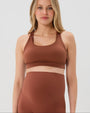 Pregnant woman wearing an AXK brown high-impact, racerback, maternity and nursing sports bra and matching high-waist maternity leggings. She has her hands cradling her belly standing in front of a white background. Premium maternity athletic and activewear by AXK - high quality petite, tall, and plus size maternity. 