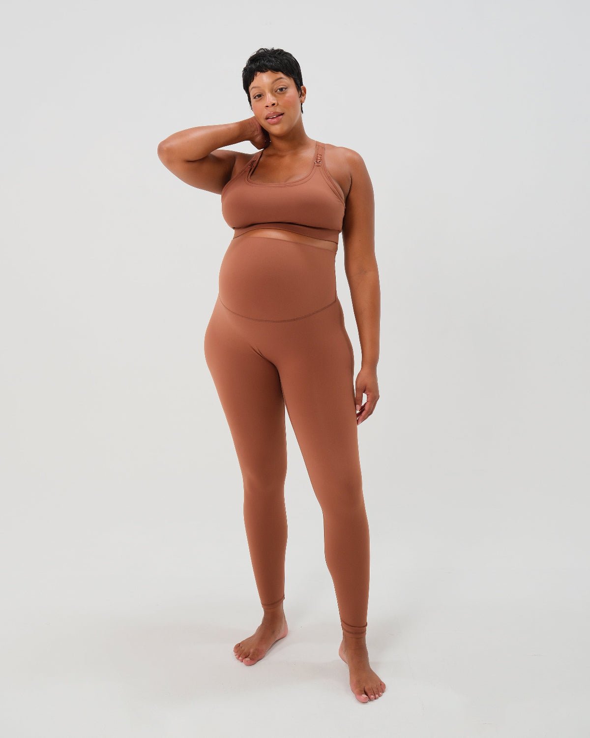 Pregnant woman wearing premium brown maternity leggings with a flattering scrunch butt and matching high-impact, racerback nursing sports bra, standing against a white background. Premium maternity athletic and activewear by AXK.