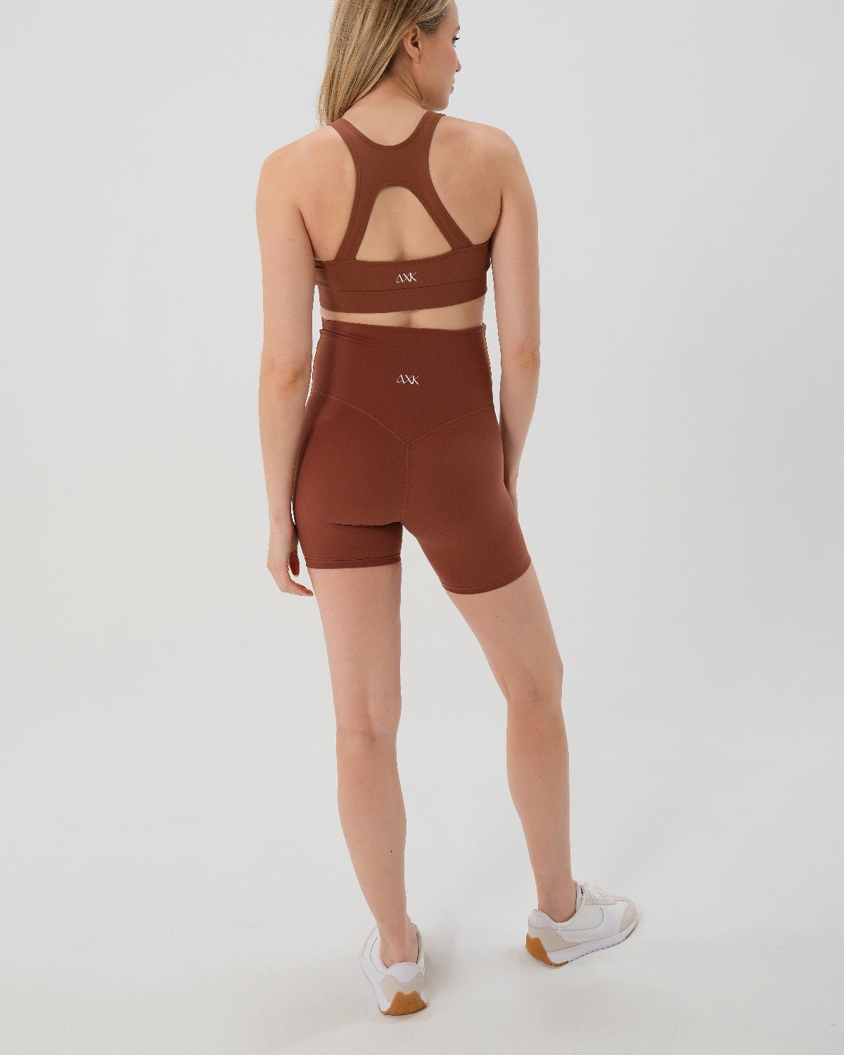 Pregnant woman wearing premium brown maternity bike shorts with a supportive high waist and matching high-impact, racerback maternity and nursing sports bra, standing against a white background. Premium maternity athletic and activewear by AXK - high quality petite, tall, and plus size maternity. 