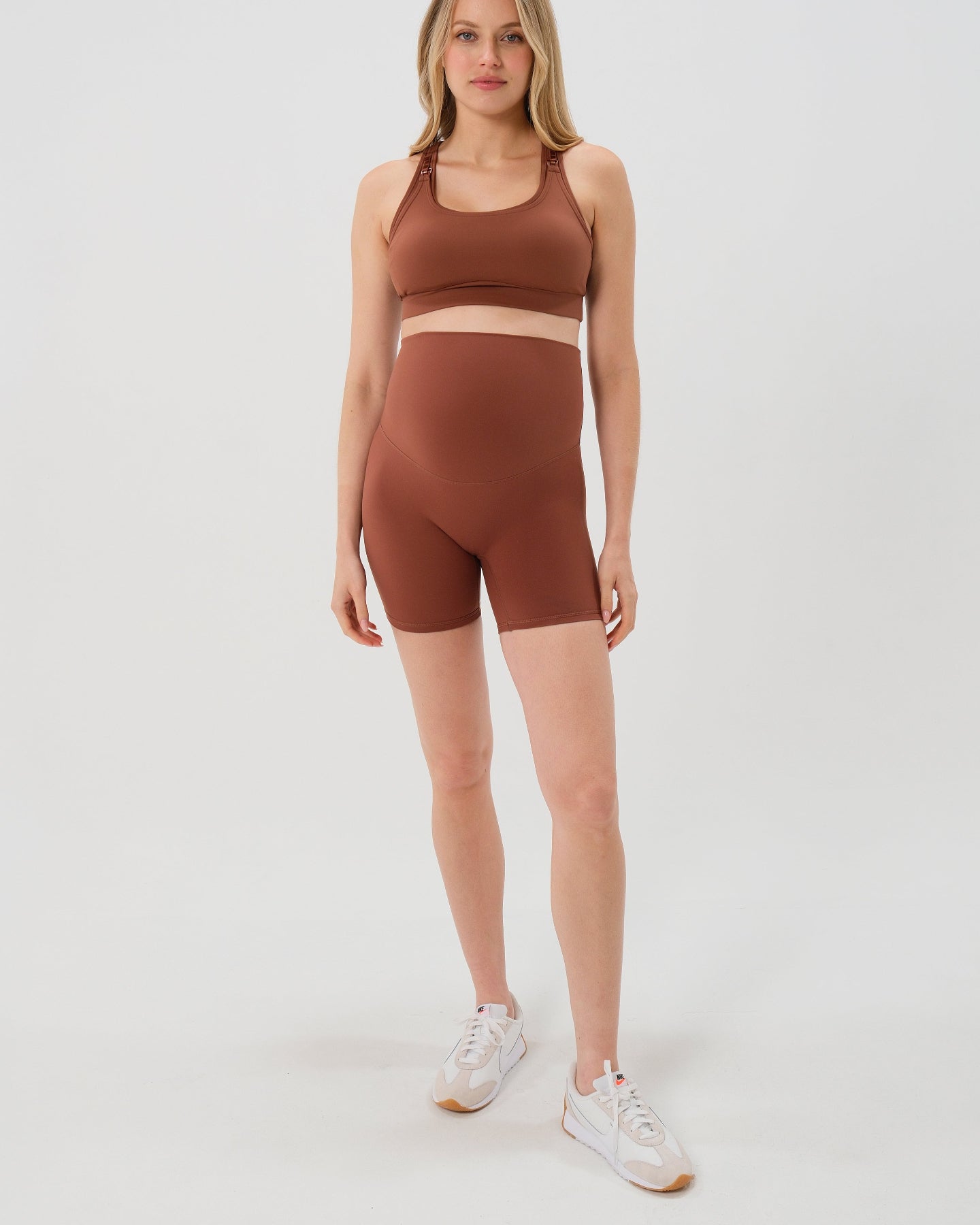Pregnant woman wearing premium brown maternity bike shorts with a supportive high waist and matching high-impact, racerback maternity and nursing sports bra. Best reviewed 2026 premium maternity athletic and activewear by AXK, petite and tall friendly, in regular and plus size options.