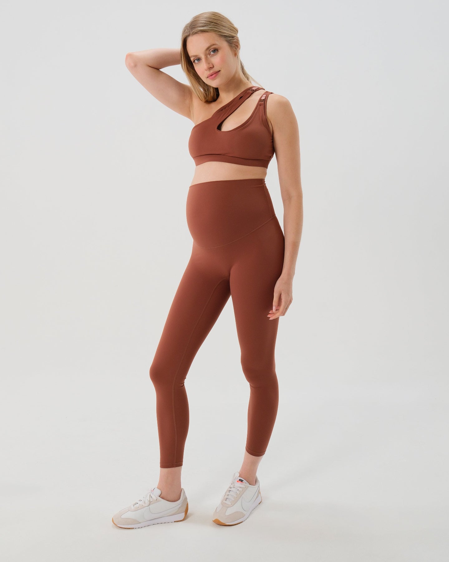 Pregnant model wearing premium brown AXK maternity leggings with a supportive high waist, bum flattering back v seam, seamless front design, and butter soft stretch fabric. Best selling with glowing 5-star reviews, these leggings are perfect for running, pregnancy yoga, walking, biking, or loungewear. High quality 2026 maternity athletic and activewear in regular and plus sizes. Petite and tall friendly. 