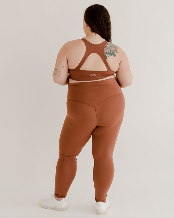 Back view of a pregnant woman wearing premium brown maternity leggings with a supportive high waist and matching high-impact racerback maternity and nursing sports bra, standing against a white background. Premium maternity athletic and activewear by AXK.