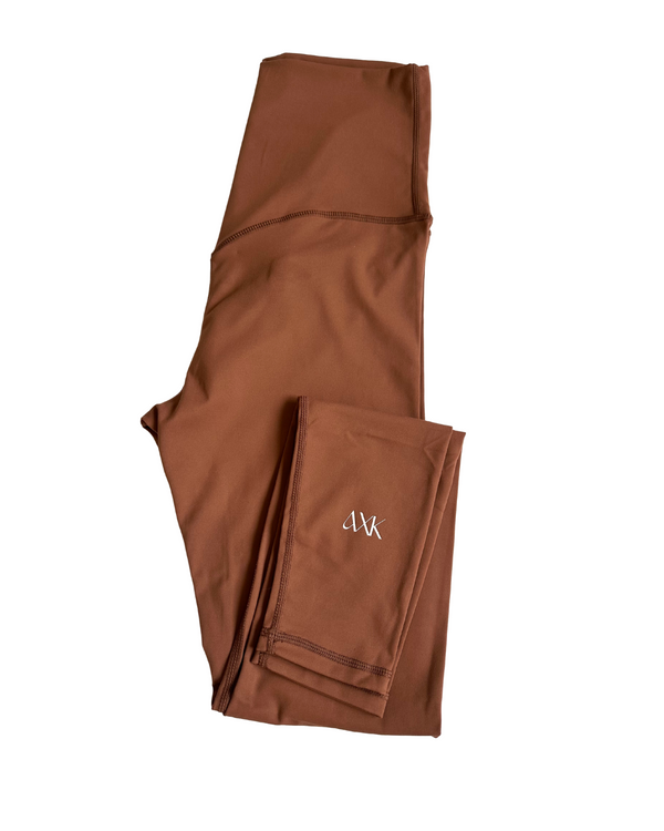 Flat lay of premium brown maternity leggings with a supportive high waist and V-seam back detail, featuring the AXK logo on the ankle, displayed on a white background. Premium maternity athletic and activewear by AXK.