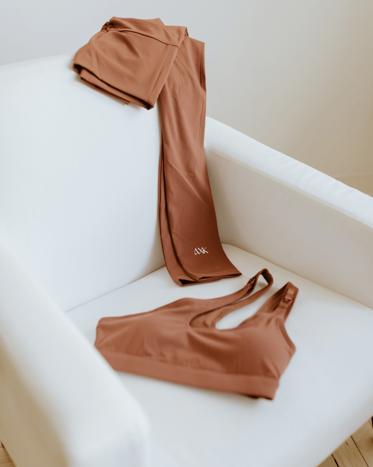 Brown one-shoulder, maternity sports bra and maternity leggings displayed on a white armchair. AXK premium maternity activewear.