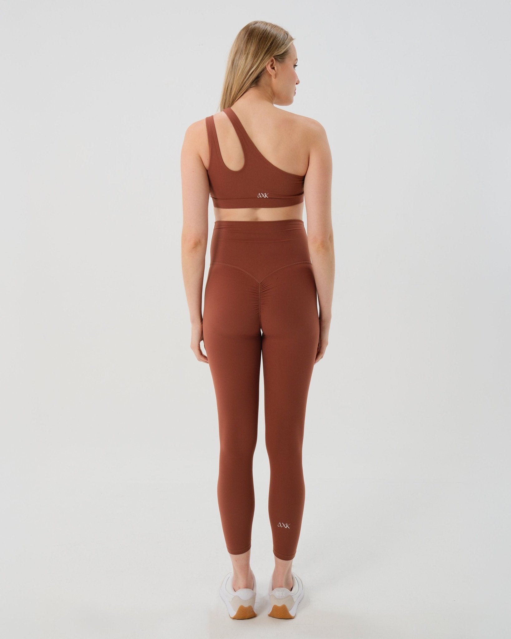 Pregnant woman wearing premium brown maternity leggings with a flattering scrunch butt and matching high-impact, racerback nursing sports bra, standing against a white background. Premium maternity athletic and activewear by AXK.