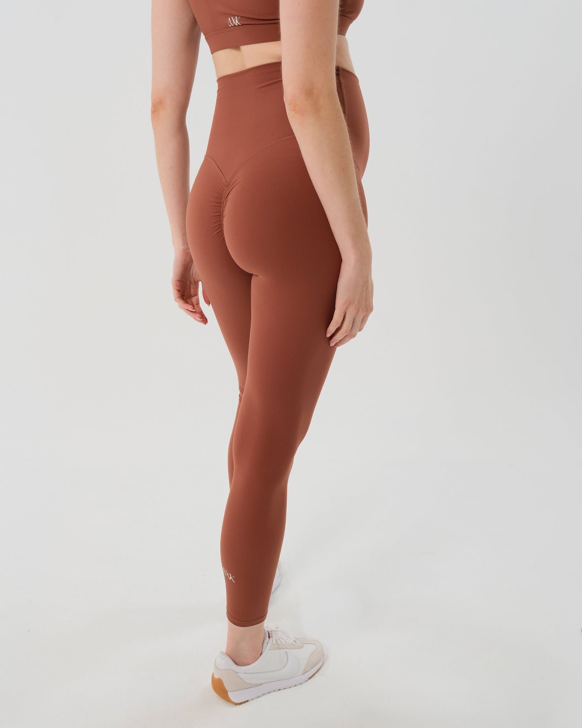 Pregnant woman wearing premium brown maternity leggings with a flattering scrunch butt and matching high-impact, racerback nursing sports bra, standing against a white background. Premium maternity athletic and activewear by AXK.