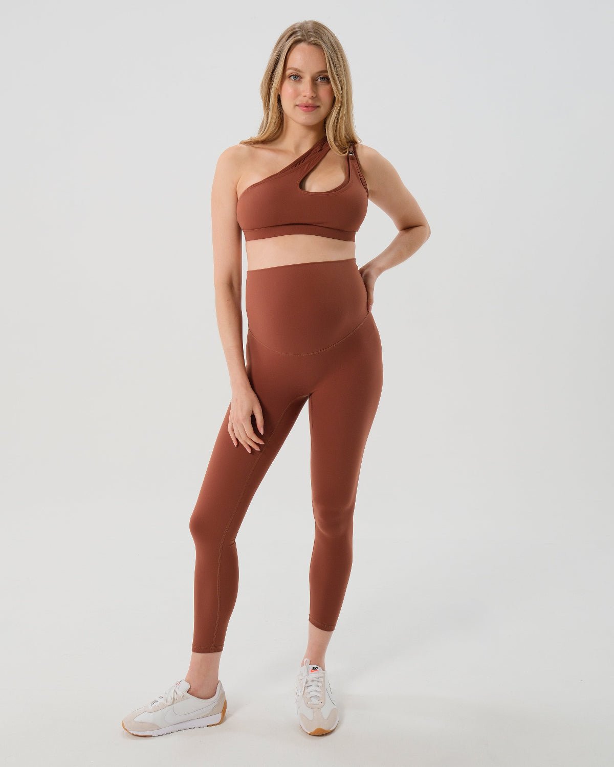 Pregnant woman wearing premium brown maternity leggings with a flattering scrunch butt and matching high-impact, racerback nursing sports bra, standing against a white background. Premium maternity athletic and activewear by AXK.