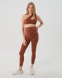 Pregnant woman wearing premium brown maternity leggings with a flattering scrunch butt and matching high-impact, racerback nursing sports bra, standing against a white background. Premium maternity athletic and activewear by AXK.