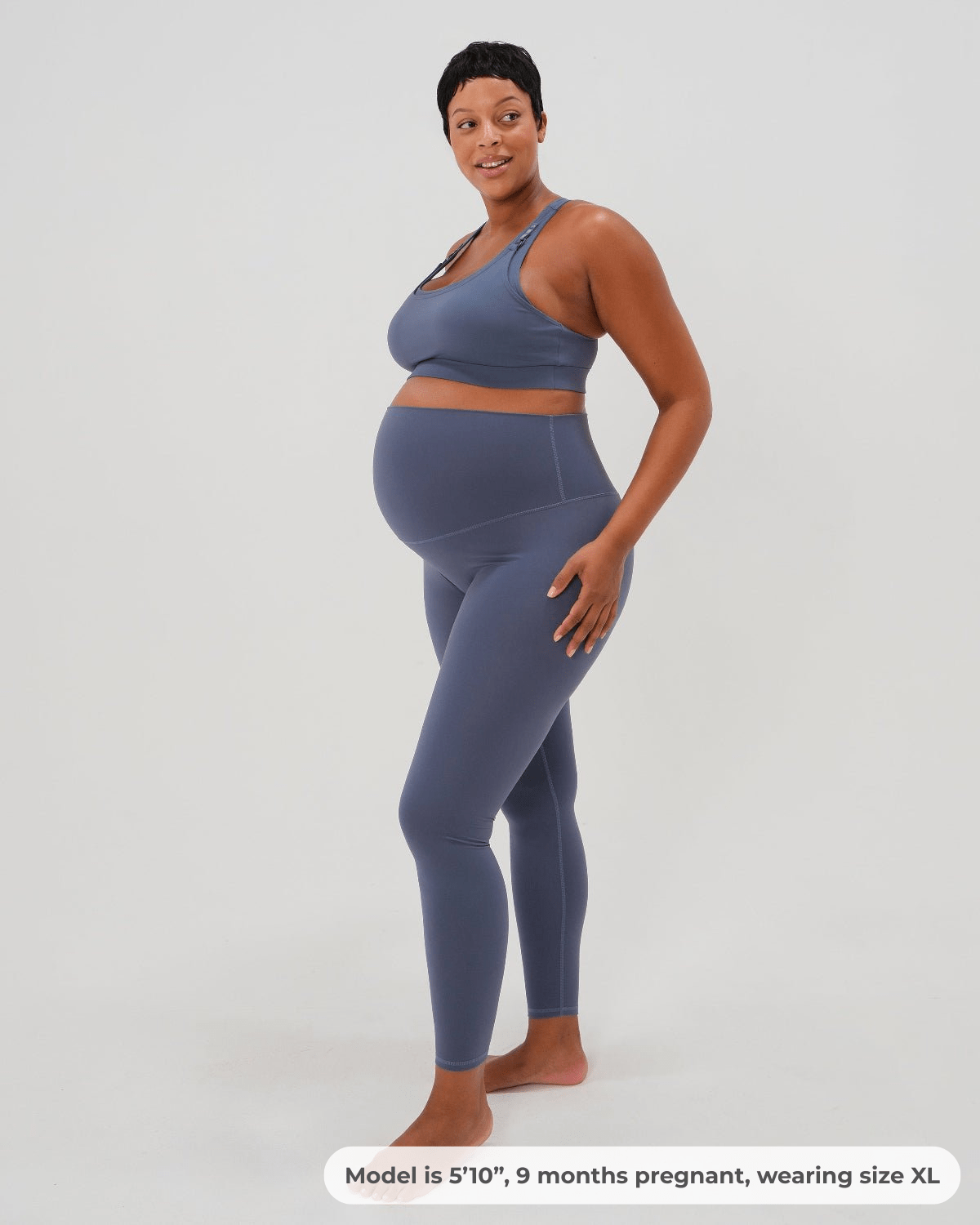 Plus size pregnant woman wearing premium blue maternity leggings with a flattering scrunch butt and matching high-impact, racerback nursing sports bra, standing against a white background. Premium maternity athletic and activewear by AXK.