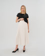 Pregnant woman wearing a modest off-white cream pleated designer maternity maxi maternity skirt in luxurious TENCEL satin by MARION. This luxury skirt can be worn over or under your belly bump. It fastens with a zip, and features deep functional pockets and a flexible elastic waistband for comfort. This refined, timeless style epitomizes quiet luxury. Perfect for maternity work wear, wedding guest dress, occasion wear, pregnancy street style, and baby shower outfits. Petite and tall friendly.