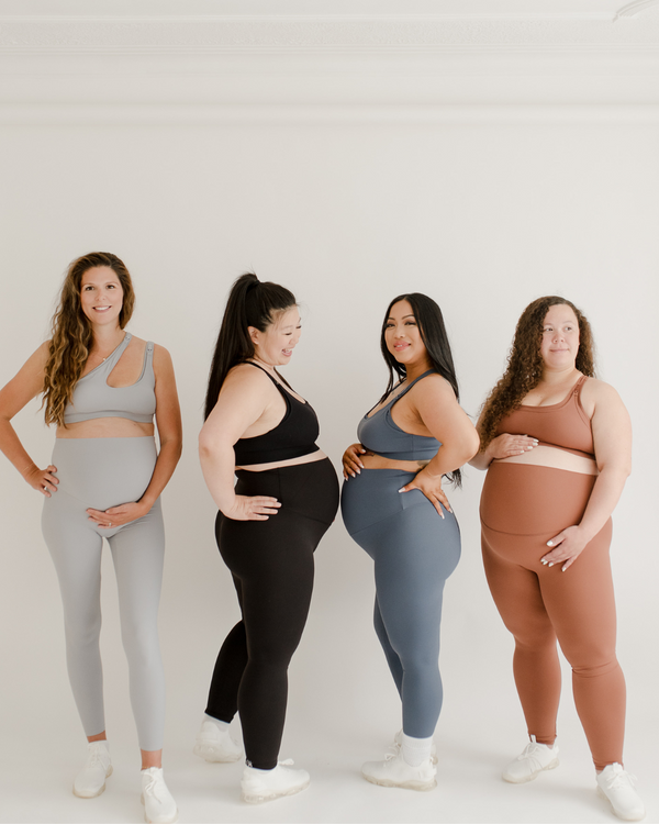 Four pregnant women of diverse body types wearing premium maternity leggings with flattering V-seam backs and matching high-impact, maternity and nursing sports bras in light grey, black,  blue, and brown. All standing against a white background. Premium maternity athletic and activewear by AXK.