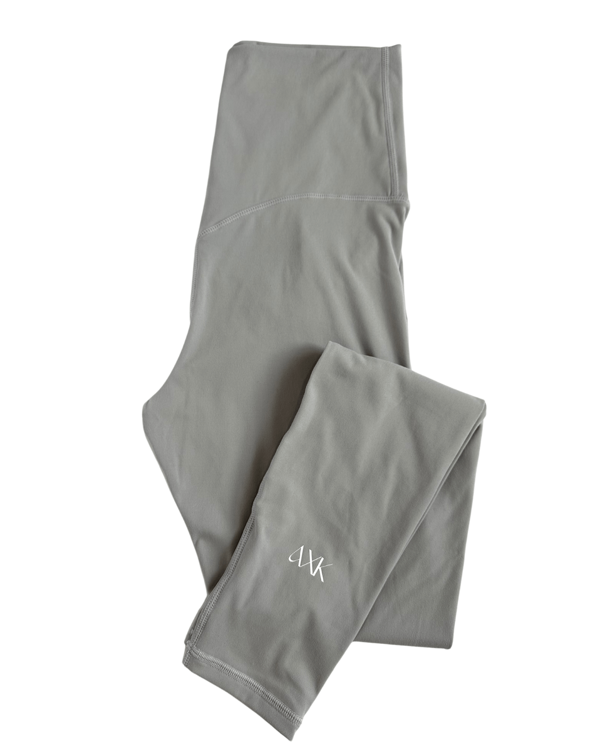 Flat lay of premium light grey maternity leggings with a flattering V-seam back and AXK logo detail on the ankle, displayed on a white background. Premium maternity athletic and activewear by AXK.