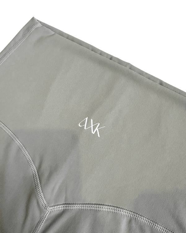 Close-up of premium light grey maternity leggings featuring the AXK logo and flattering V-seam detail, displayed on a white background. Premium maternity athletic and activewear by AXK.