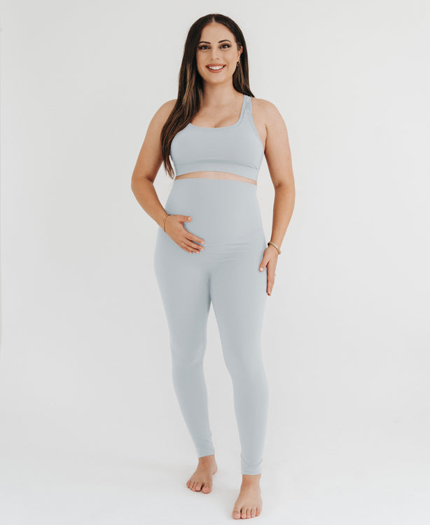 Pregnant woman wearing premium light grey maternity leggings with a flattering scrunch butt and supportive high waist and a high impact, racer back nursing sports bra on a white background. Premium maternity athletic and activewear by AXK.