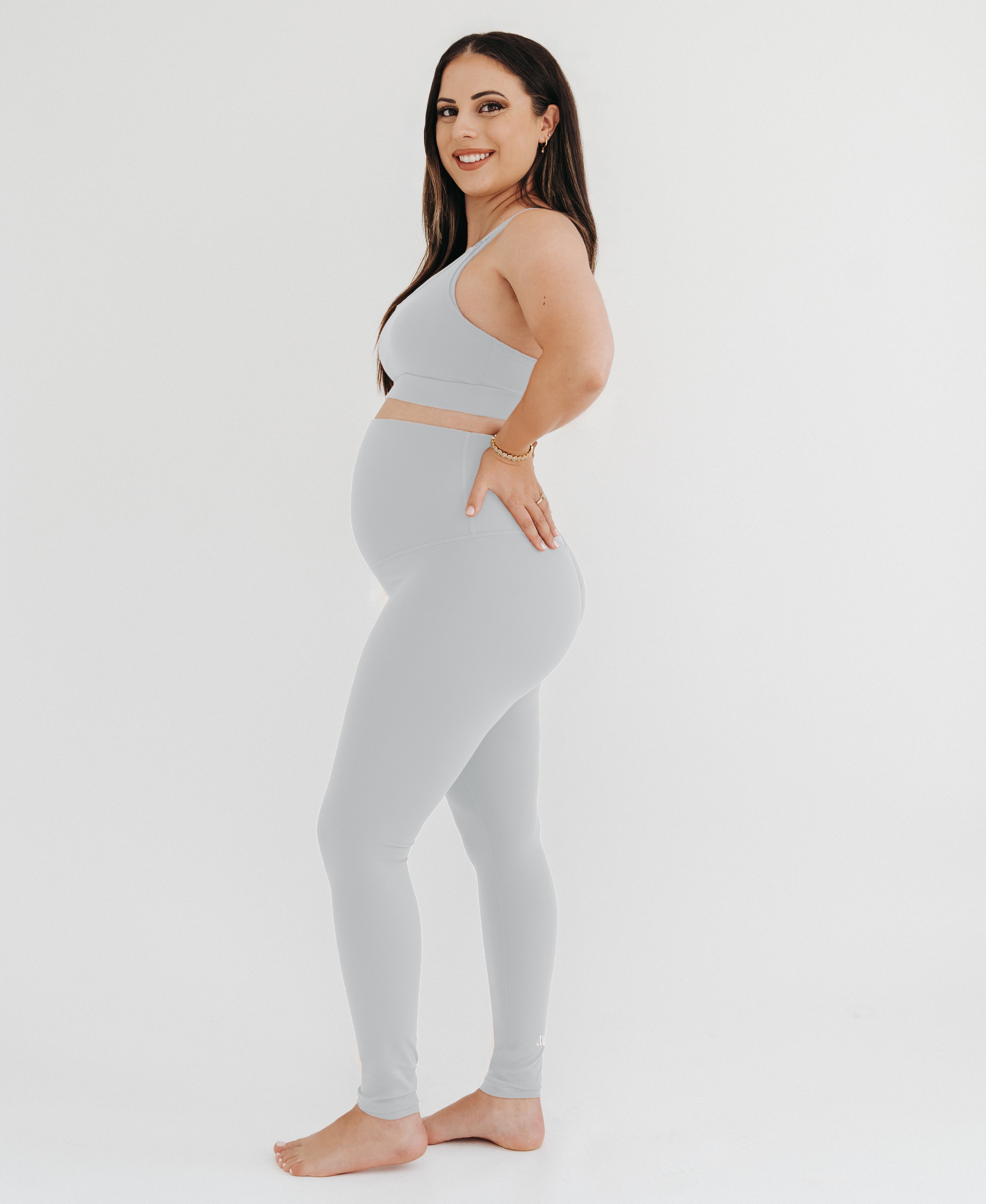 Pregnant woman wearing premium light grey maternity leggings with a flattering scrunch butt and a high impact, racer back nursing sports bra on a white background. Premium maternity athletic and activewear by AXK.