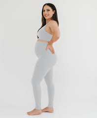 Pregnant woman wearing premium light grey maternity leggings with a flattering scrunch butt and a high impact, racer back nursing sports bra on a white background. Premium maternity athletic and activewear by AXK.