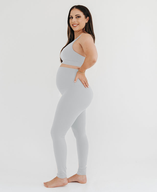 Pregnant woman wearing premium light grey maternity leggings with a flattering scrunch butt and a high impact, racer back nursing sports bra on a white background. Premium maternity athletic and activewear by AXK.