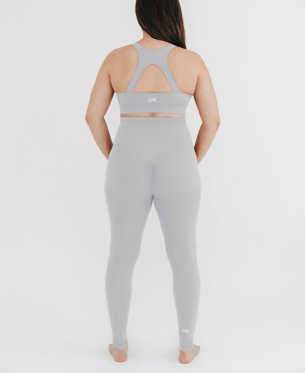 Pregnant woman wearing premium light grey maternity leggings with a flattering scrunch butt and a high impact, racer back nursing sports bra on a white background. Premium maternity athletic and activewear by AXK.