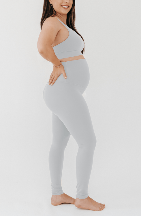 Pregnant woman wearing premium light grey maternity leggings with a flattering scrunch butt and a high impact, racer back nursing sports bra on a white background. Premium maternity athletic and activewear by AXK.