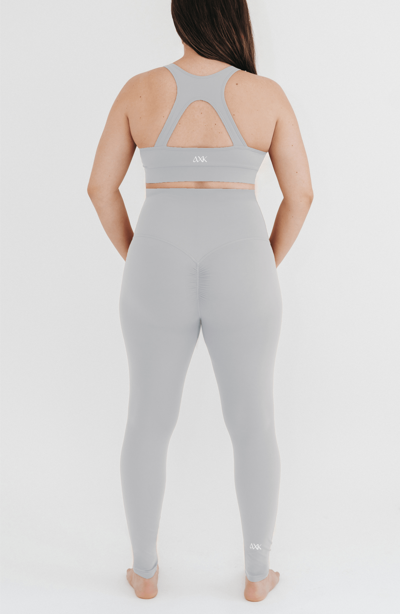 Pregnant woman wearing premium light grey maternity leggings with a flattering scrunch butt and a high impact, racer back nursing sports bra on a white background. Premium maternity athletic and activewear by AXK.
