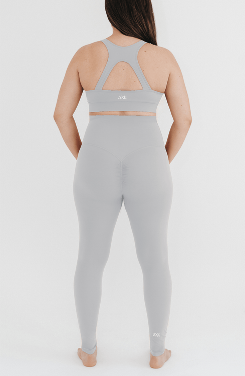 Pregnant woman wearing premium light grey maternity leggings with a flattering scrunch butt and a high impact, racer back nursing sports bra on a white background. Premium maternity athletic and activewear by AXK.