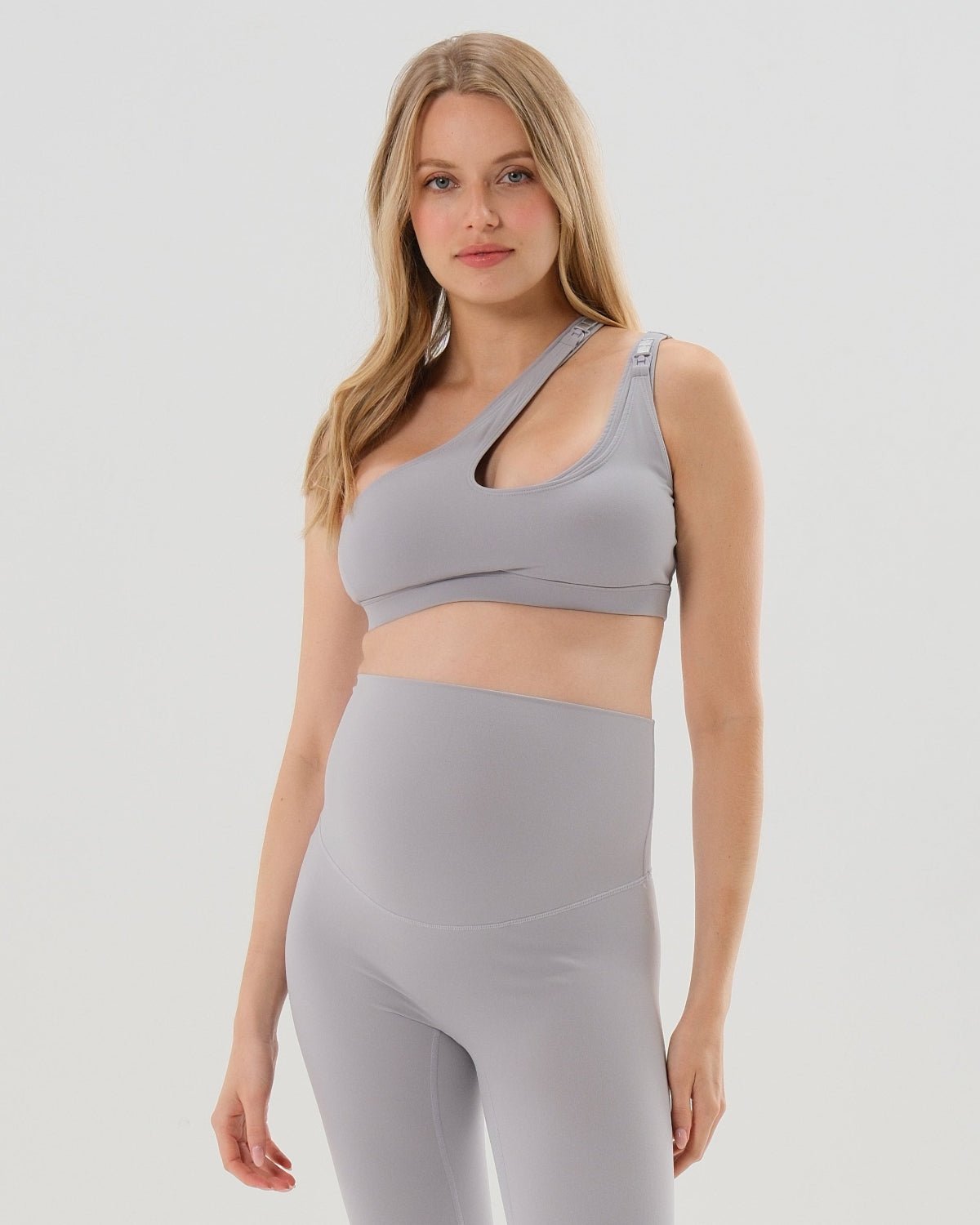 Light gray one-shoulder maternity and nursing sports bra and matching leggings. The bra features one-handed clip access for easy breastfeeding. Premium maternity activewear by AXK is offered in petite and plus size. 
